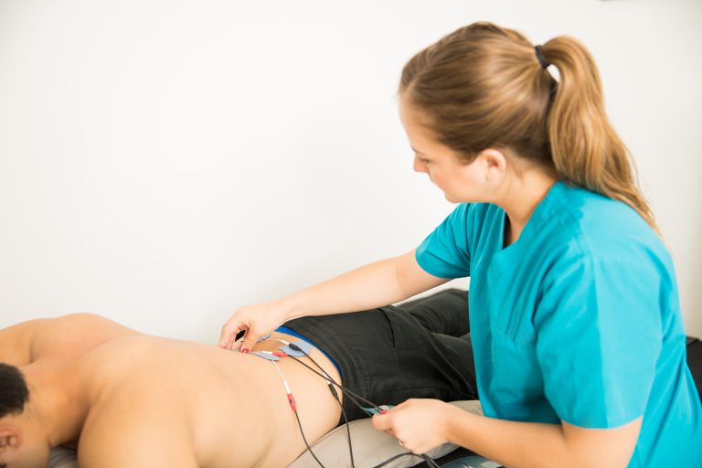Therapist Positioning Electrodes On Customer For Lower Back Muscle Treatment